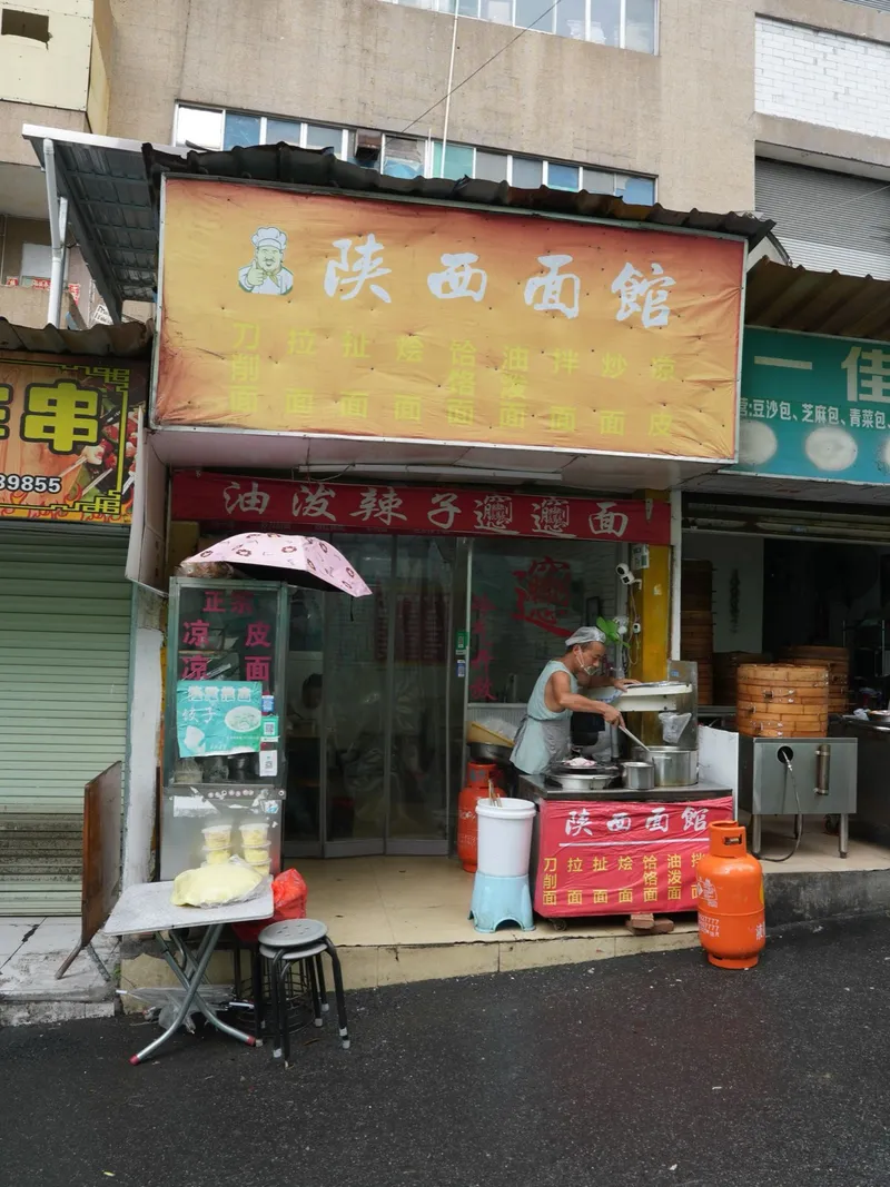A Shaanxi noodle house storefront with biangbiang noodle signage and a cook at the counter