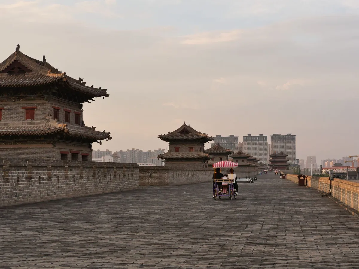 Riders on the wide brick top of Xi'an's City Wall at dusk, with watchtowers ahead