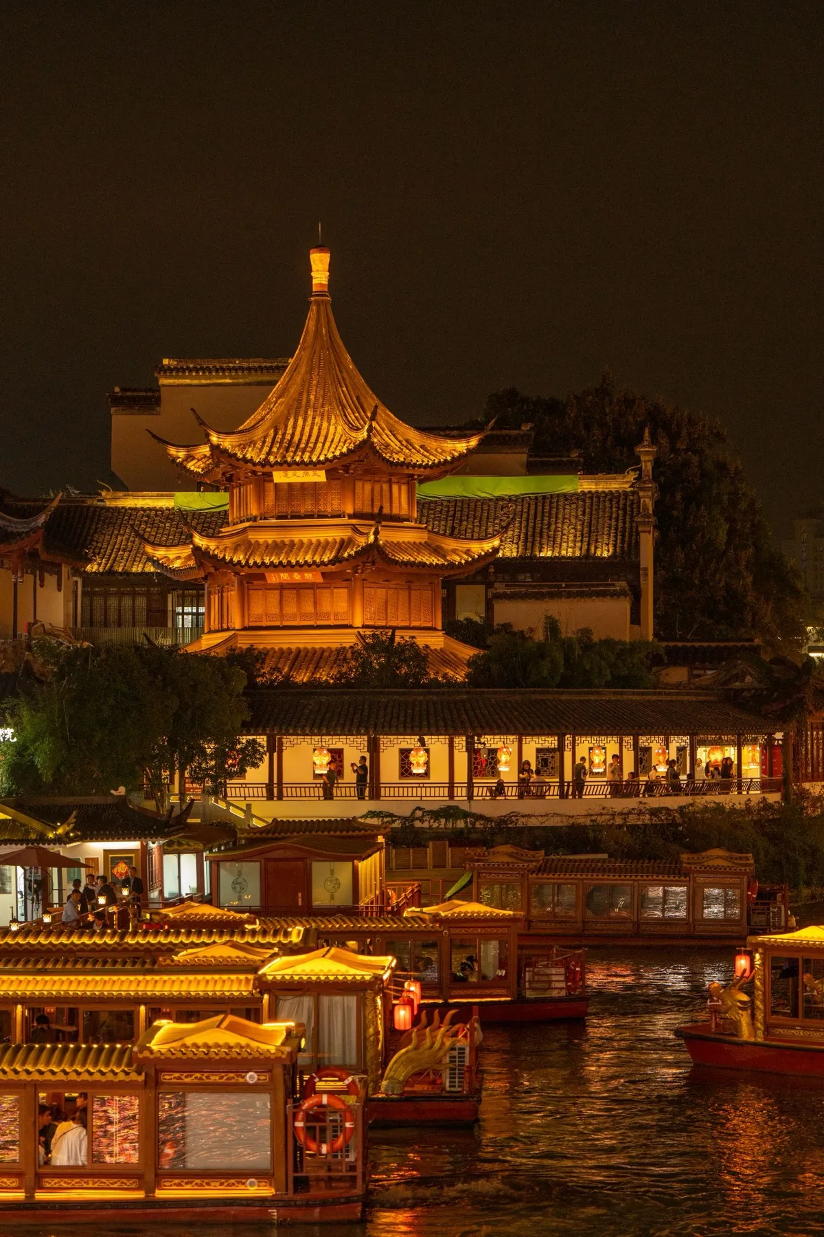 A golden illuminated pagoda beside the Qinhuai River with lantern-lit boats at night