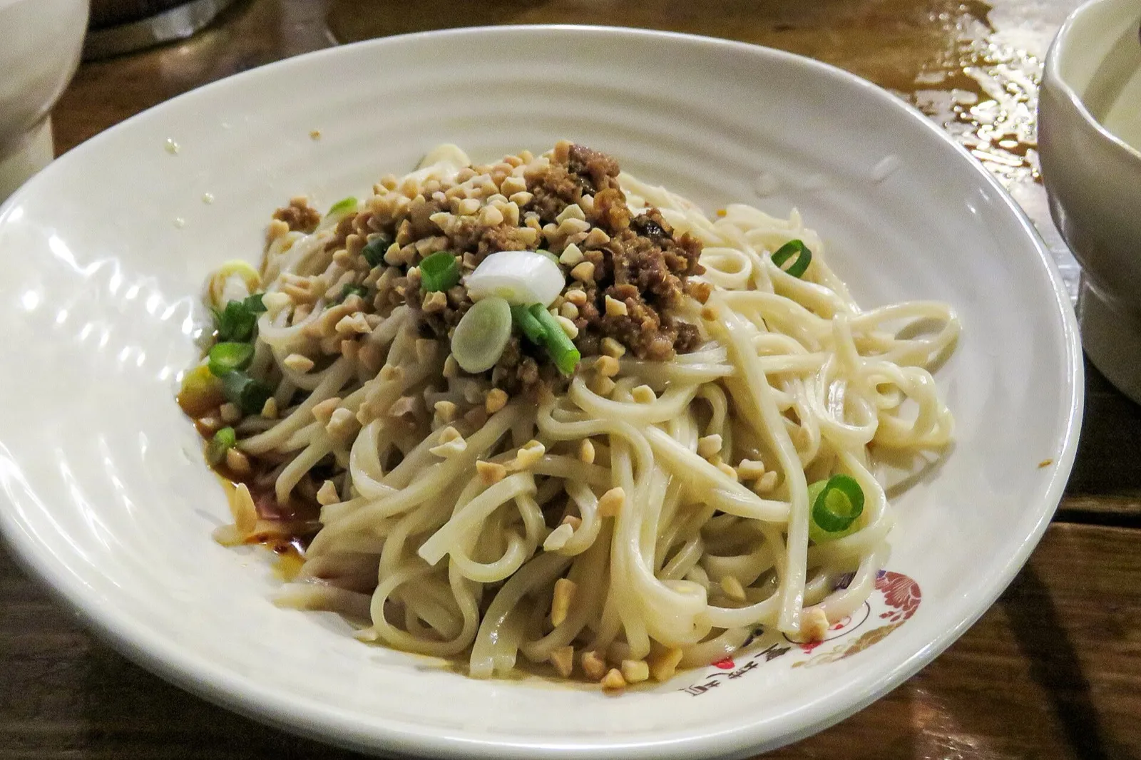 A bowl of dan dan noodles topped with minced pork, peanuts, and scallions