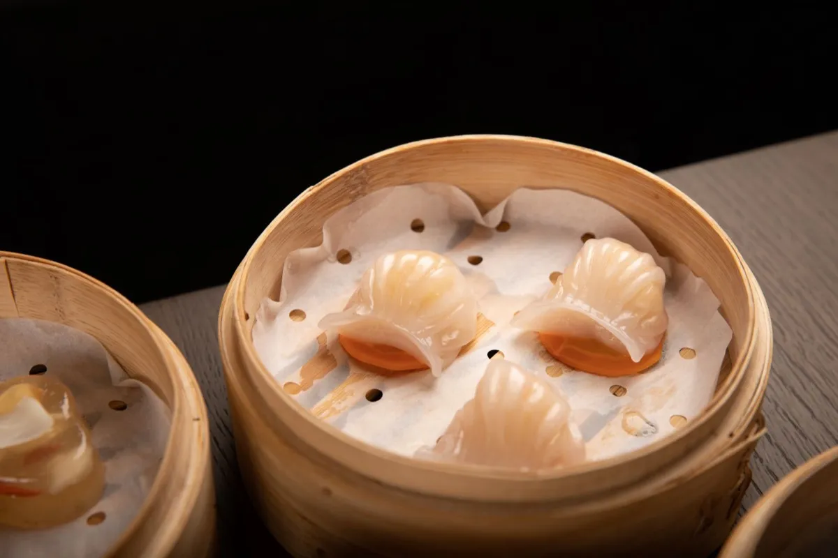 Three pleated translucent har gow shrimp dumplings in a bamboo steamer basket