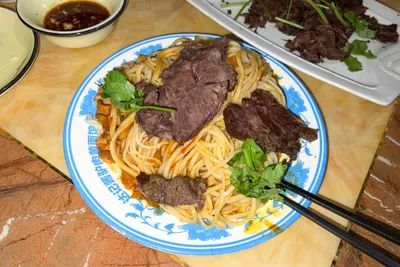 A plate of yellow hand-pulled noodles topped with sliced braised donkey meat and cilantro
