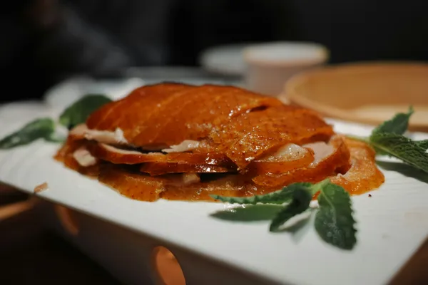 Slices of crisp-skinned Peking duck plated with herbs