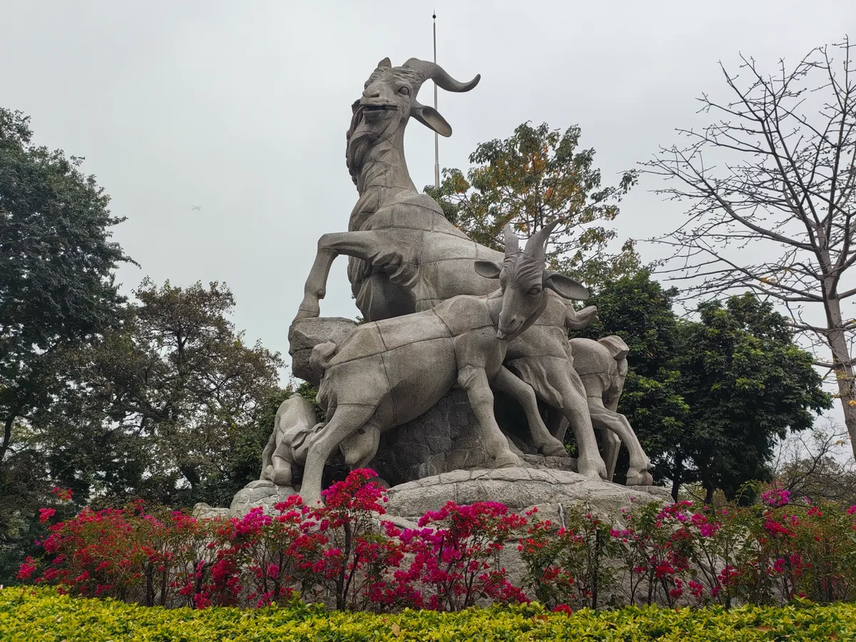 The granite Five Rams Statue surrounded by flowering shrubs in Yuexiu Park