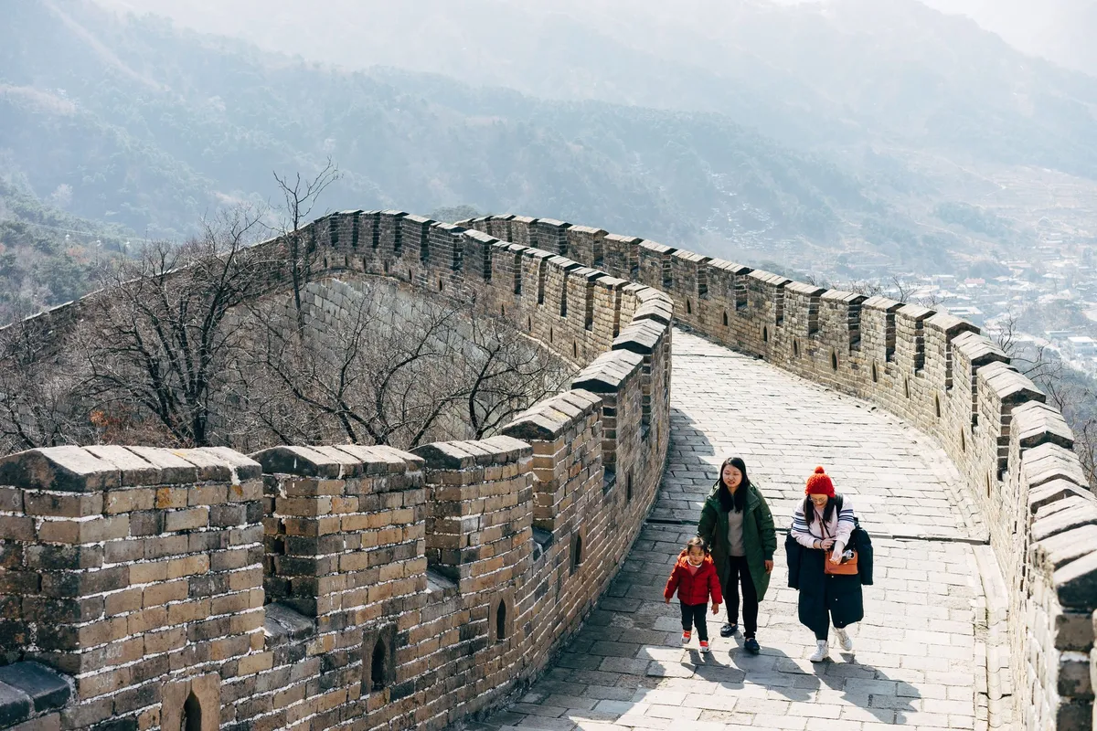 A quiet, near-empty walkway on the Great Wall in winter, with a small family walking and mountains in the haze beyond