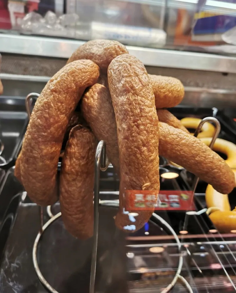 Reddish-brown smoked sausages hanging on display hooks at a Harbin deli counter