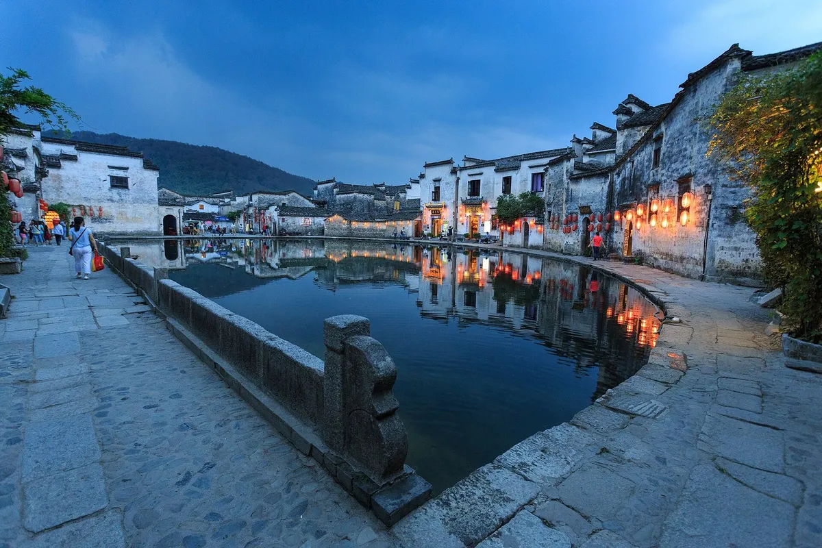 Hongcun's Moon Pond at blue hour, with lantern-lit Hui houses reflected in the water