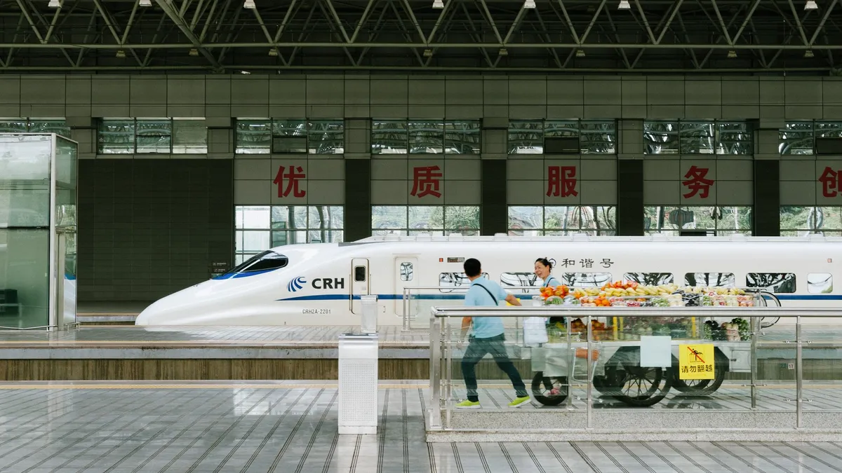 A CRH high-speed train stopped at a station platform in Yichang, with a fruit vendor cart and a passenger walking past