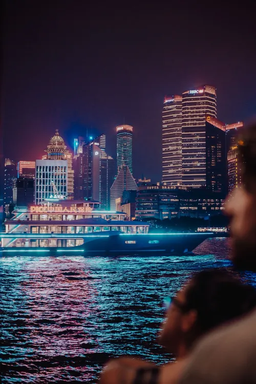 A river cruise boat passing the illuminated Shanghai skyline at night