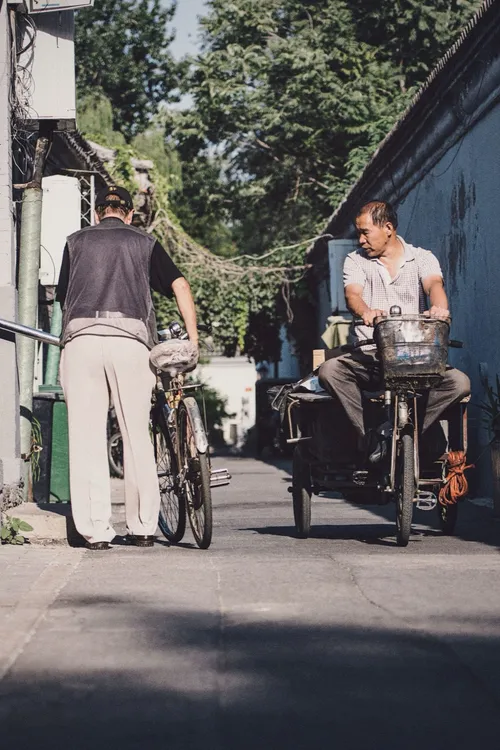Residents with bicycles and a cargo tricycle in a narrow Beijing hutong lane