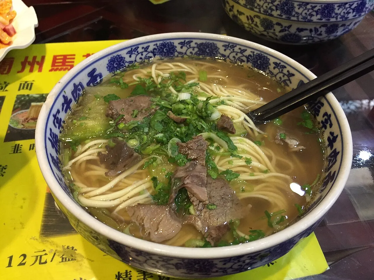A bowl of Lanzhou beef noodles with sliced beef, cilantro, and scallion in clear broth