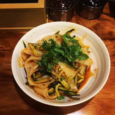 A bowl of cold liangpi noodles tossed with cucumber, cilantro, and chili oil