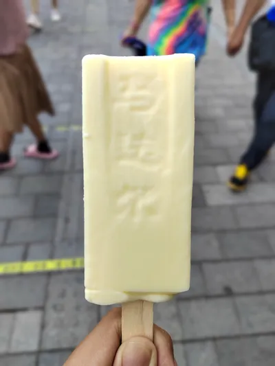 A hand holding a pale yellow Modeler ice cream bar with embossed lettering, Central Street in the background