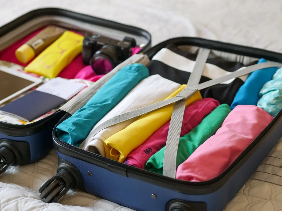 An open suitcase packed with rolled clothes, a camera, passport, and boarding pass