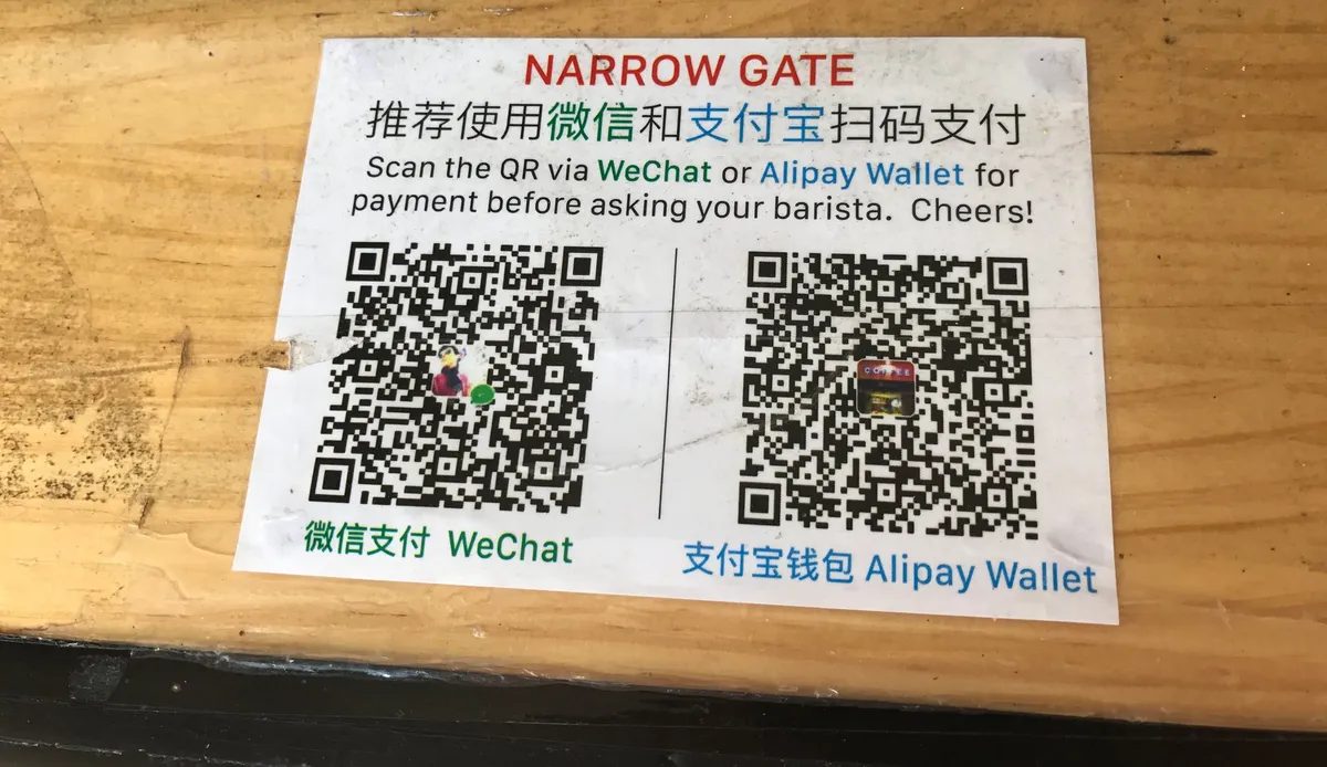 A bilingual sign showing WeChat Pay and Alipay Wallet QR codes for scanning at a counter