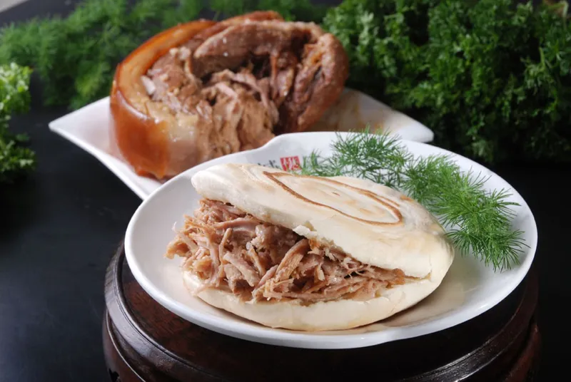 A whole braised pork roujiamo cut open next to the meat it's made from