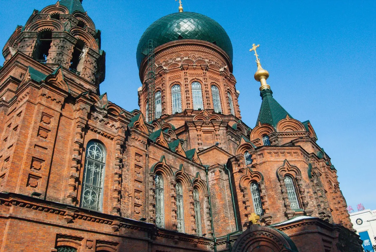 The red-brick Saint Sophia Cathedral with its green onion dome and golden cross against a blue sky