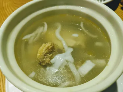 A clay-pot bowl of coconut chicken hotpot with chicken, mushrooms, and taro in clear coconut broth