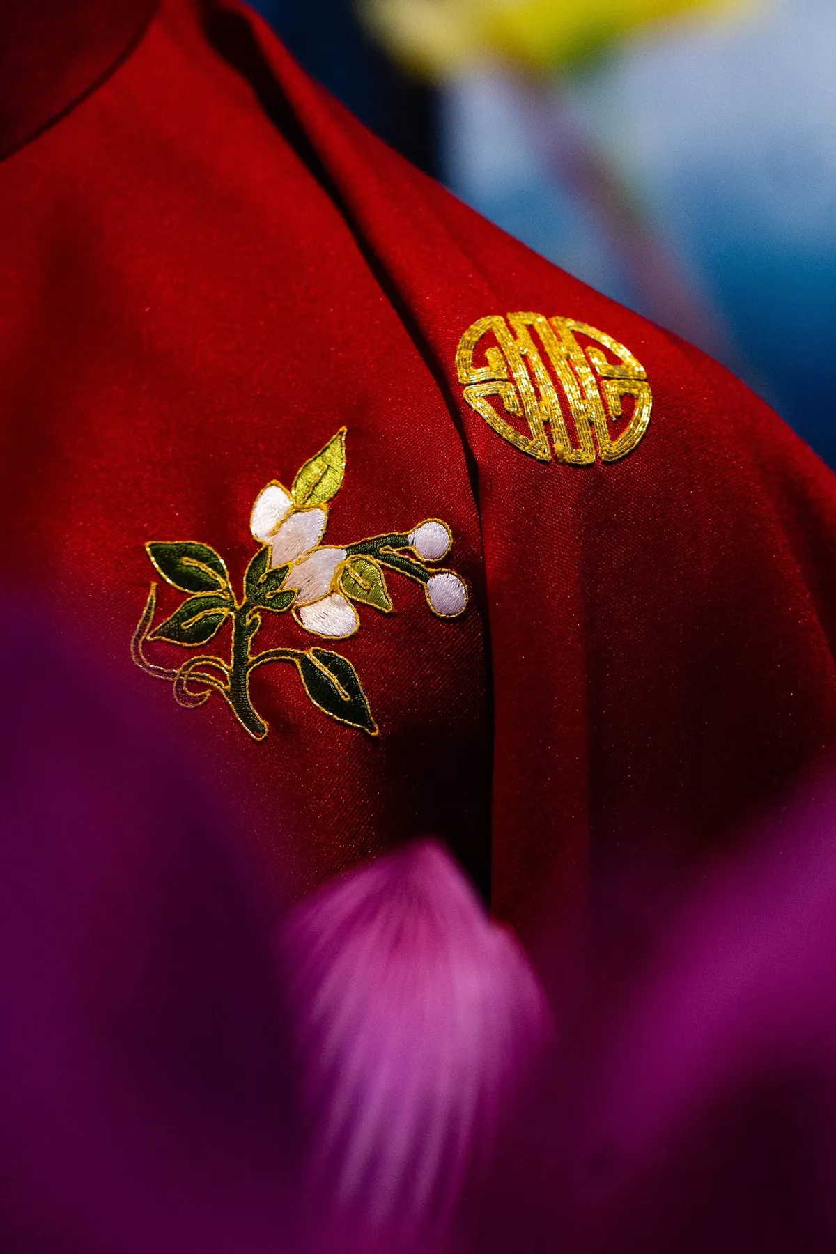 A close-up of a red silk garment with fine gold and floral hand embroidery
