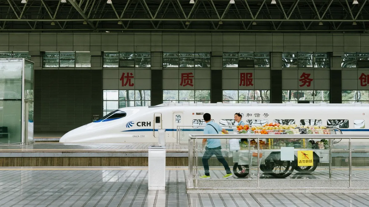 A CRH high-speed train at a platform while a vendor pushes a fruit cart past