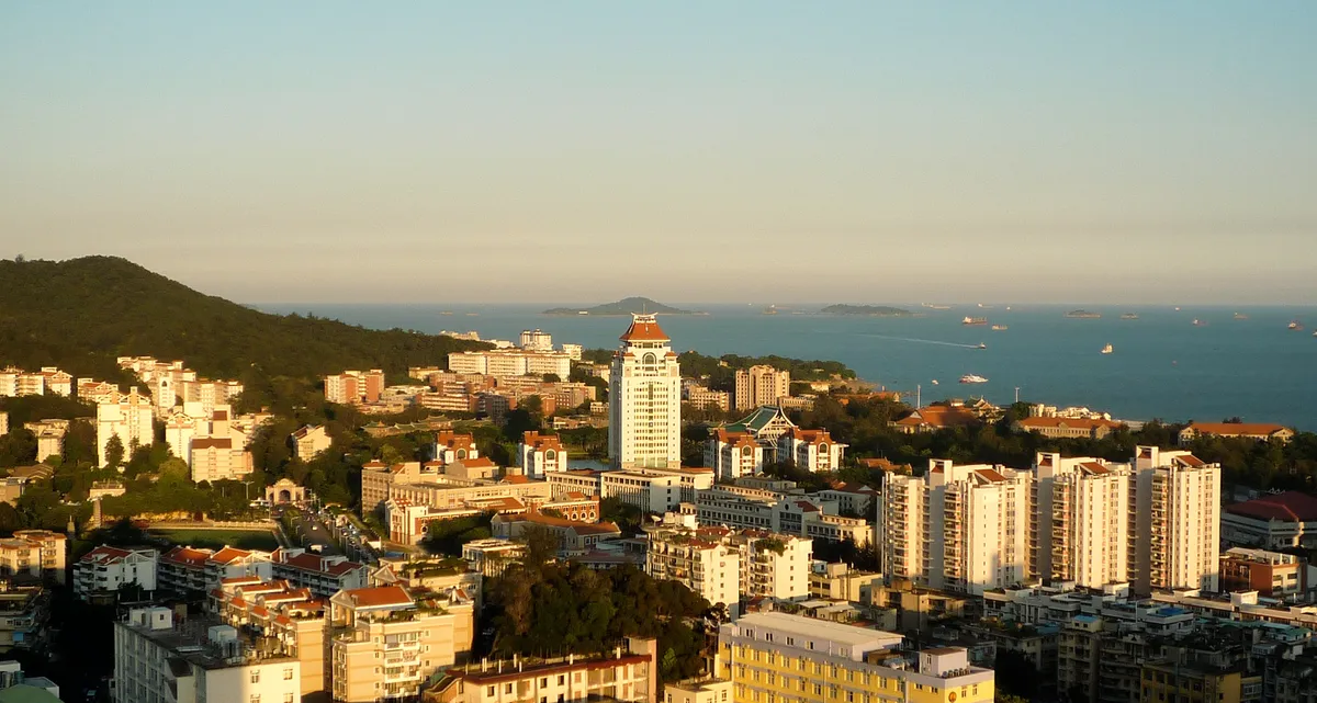 An aerial sunset view of Xiamen University's red-roofed campus buildings beside the sea