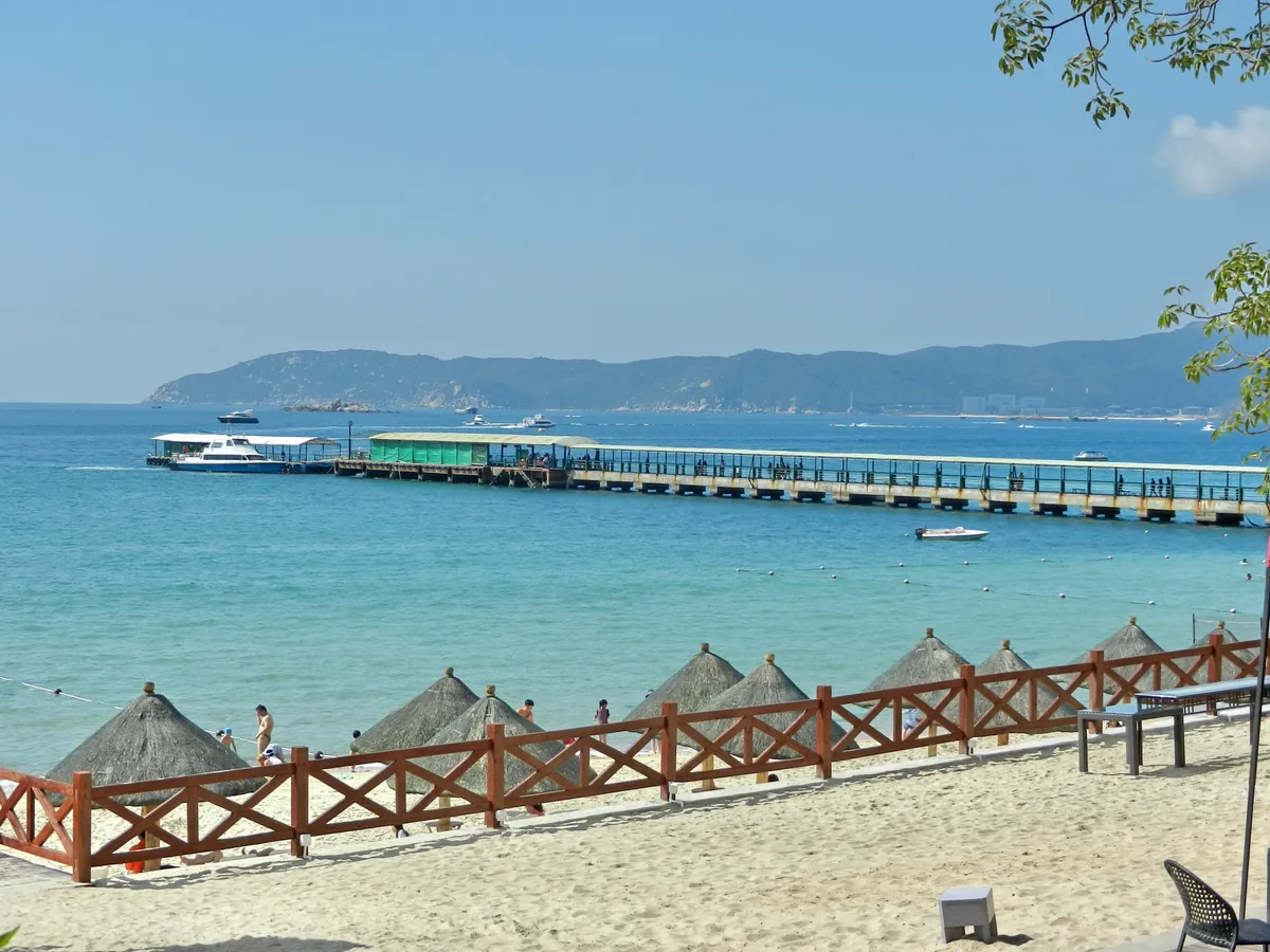 Turquoise water, thatched beach umbrellas, and a pier at Yalong Bay, Sanya